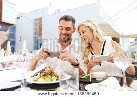 love, date, technology, people and relations concept - happy couple with smatphone taking picture of food at restaurant terrace