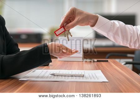 Real estate concept. Realtor is passing keys to the client sitting behind desk with contract on blurred background.
