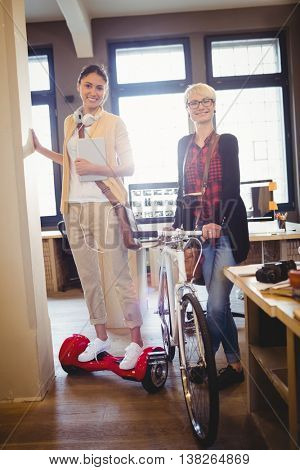 Graphic designer holding bicycle while colleague standing on hover board in office