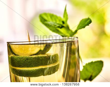 Alcohol drink. On wooden boards is glass with alcohol green transparent drink. A drink number hundred fifty one cocktail mohito with slice lime and mint . Country life. Outdoor. Light background.