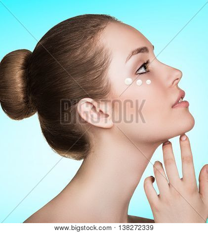 Beautiful model applying cosmetic cream dots on her face over blue background
