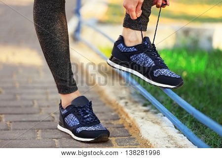 Woman in sportswear tying shoelaces on sneakers outdoor close-up