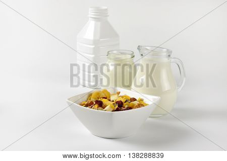 bowl of oat flakes with jug of milk and glass of white yogurt on off-white background with shadows