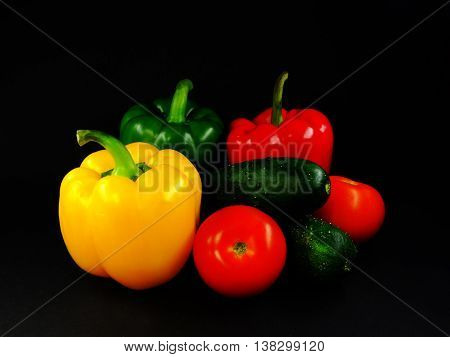 composition still life on a black background three peppers, two cucumbers and two tomatoes