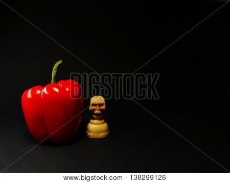 red pepper and chess pawn with a skull on a black background