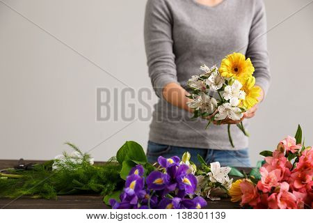 Girl in gray blouse and jeans make bouquet of herberas and alstroemerias over gray background, flowers on wood table.