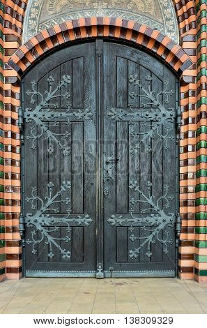 Massive wooden church door with a handle forged with an iron grip settled into a brick wall at the church. Breclav. South Moravia