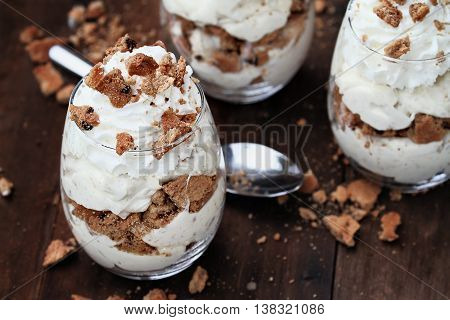 Three glasses of crumbled chocolate chip cookies and cheesecake parfaits against a rustic background. Extreme shallow depth of field with selective focus on dessert in front.