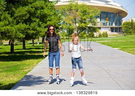Learning mother and daughter on roller skates in summer