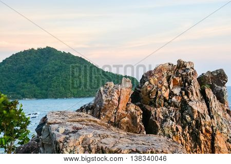 A scenery of sea at the sunset time with a rock and leaves at the bottom and a mountain at a side of a photo in Chantgaburi Thailand.