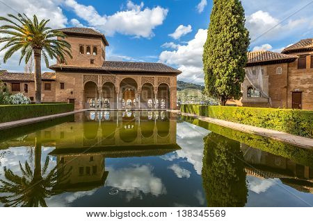 El Partal in Alhambra of Granada, Unesco Heritage Site, Andalusia, Spain. A large central pond faces the arched portico which stands behind the Tower of the Ladies reflecting in the water.