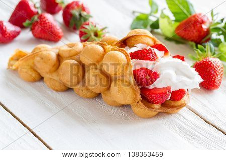 waffles with strawberries and whipped cream on the wooden table