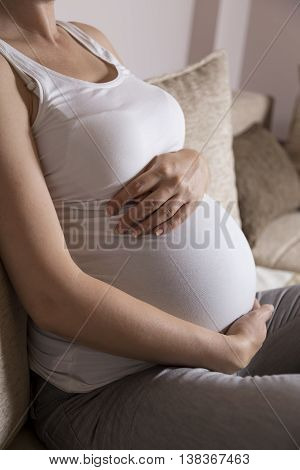 Close up of a pregnant woman's belly while she is sitting on a couch in a living room and gently touching and holding her belly