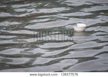 Foam bowl floating on a black river.
