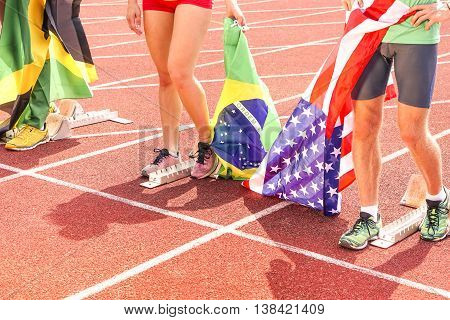 International sport athletes at stadium track holding national flags - Runners legs and feet at start grid cropped view from above - Professionals sportsmen celebrating victory of the competition