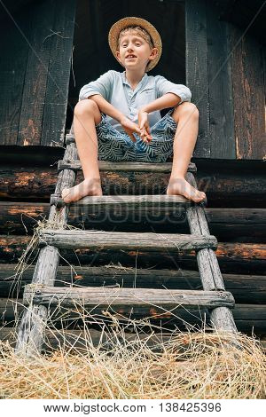 Boy sits on the ladder in hayloft