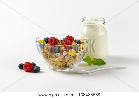 bowl of cereals and berry fruit and glass of white yogurt on off-white background with shadows