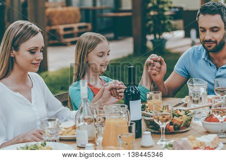 Feeling thankful for meal. Family holding hands and praying before dinner while sitting at the table outdoors