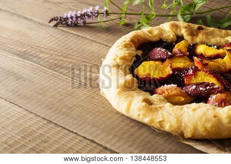 Homemade flan with plums and peaches. Delicious galette with fruits on rustic wooden background.