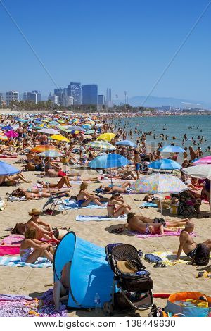 BARCELONA, SPAIN - JULY 10: Sunbathers at Platja del Bogatell beach on July 10, 2016 in Barcelona, Spain, with the Parc del Forum in the background. This busy beach is mainly frequented by the locals