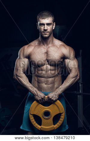 Male bodybuilder fitness model trains in the gym