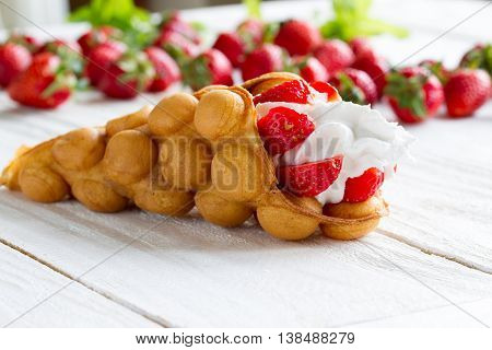 waffles with strawberries and whipped cream on the wooden table