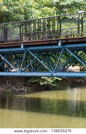 Modern wooden bridge with the metal frame is crossing the canal to the city park.