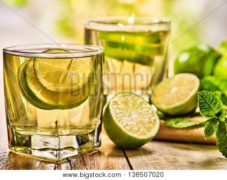 Country drink. On wooden boards are two short glasses with green transparent drink and half green lime . A drink number hundred fifty three mojito with mint leaf . Country life. Light background.