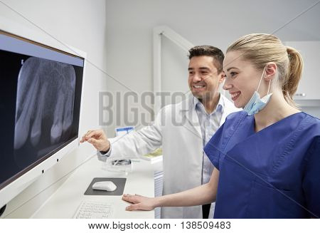 people, medicine, stomatology, technology and health care concept - happy dentists looking to x-ray scan on monitor at dental clinic