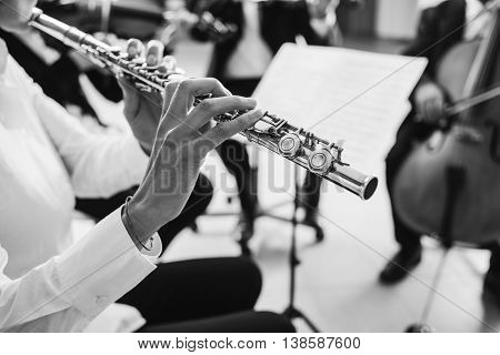 Professional female flustist playing her instrument on stage with classical music symphony orchestra