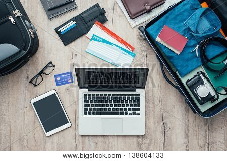 Traveler packing and getting ready for a trip desktop with baggage tickets credit card laptop and digital tablet flat lay