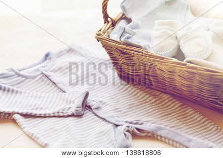 clothing, babyhood, motherhood and object concept - close up of white baby bootees with pile of clothes and towel for newborn boy in basket on table