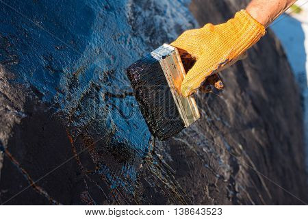 Roofer cover the concrete base polymer modified bitumen waterproofing primer. A worker brushes cover concrete bitumen-rubber primer.