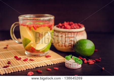 Cup of delicious dietary Goji berry tea with lime on wooden background with measuring tape. Wolfberry for a healthy diet. Alternative medicine. Recovery. Rejuvenation. Slimming. Selective Focus.
