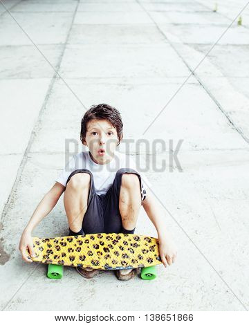 little cute boy with skateboard on playground alone training, making funy faces close up