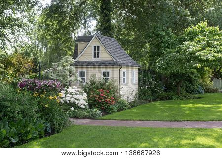 A charming playhouse sits in a shaded perennial garden.