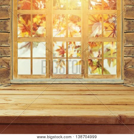Empty wooden deck table over wndow and autumn leaves bokeh background for product montage display