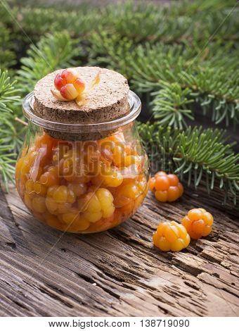 Juicy ripe cloudberry northern and sugar in a small glass jar on a wooden background