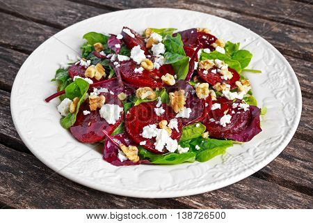 Healthy Beet Salad with fresh sweet baby spinach, kale lettuce, nuts, feta cheese on wooden table