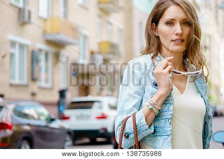 Glamorous portrait of beautiful brunette woman in blue denim jacket and white dress with sunglasses