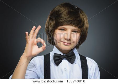 Happy boy. Closeup Portrait of handsome teenager smiling and show Ok over grey background.
