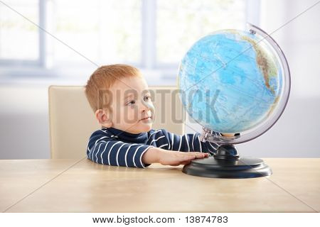 Sladký raního chlapeček studiem zeměkoule, sedící u stolu.?
