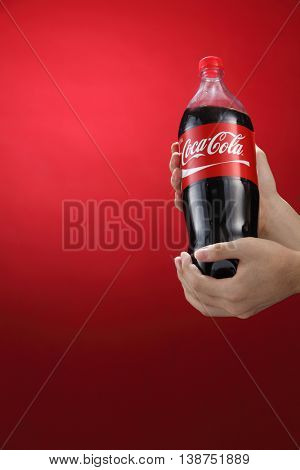 Kuala Lumpur,Malaysia 11th July 2016, Hand hold a bottle 1.5 litre Coca-Cola on red background. Coca Cola drinks are produced and manufactured by The Coca-Cola Company.
