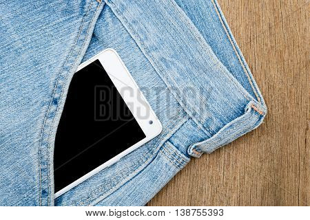 White smart phone in jeans pocket on wooden background.