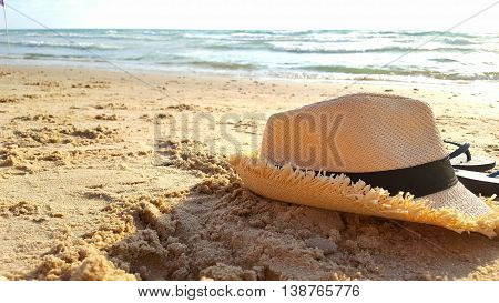 a straw hat and flip flops on the sand at the beach