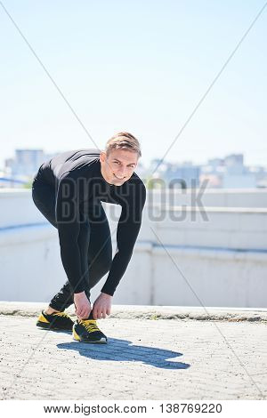 The athlete straightens his sneakers against the background of the city
