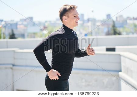 Athlete in black tight clothes runs on the background of the city and smiling