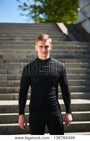 Portrait of a athletic man in a black slinky dress against the backdrop of the stairs