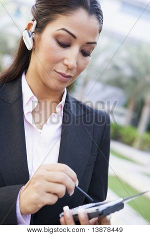 Businesswoman using PDA and earpiece outside