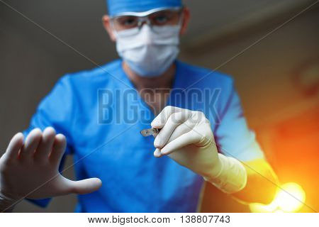 Doctor With A Scalpel Against A Bright Operating Light. Modern Surgeon Begins The Operation.